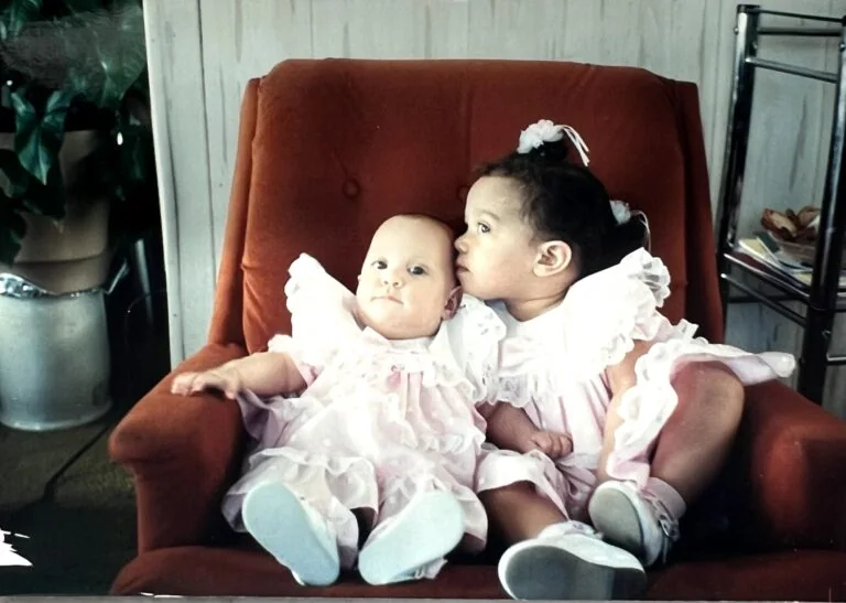 Krystle and Bethany Whitley together as young children in a rust-colored chair